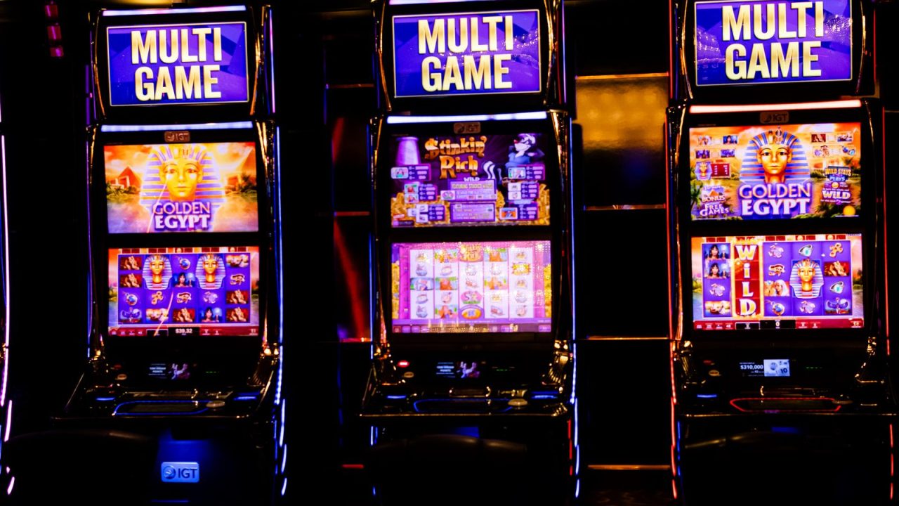 Three illuminated slot machines in a bustling casino at night.